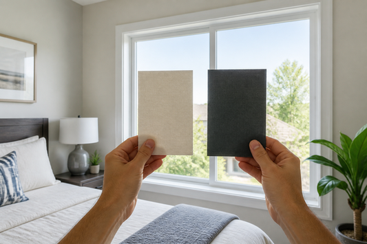 Homeowner comparing pale and dark opaque shade fabric samples at a bright bedroom window